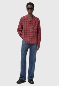 Rødternet langærmet skjorte med brystlomme, knaplukning, parret med lyseblå vide denimjeans og sorte sko.