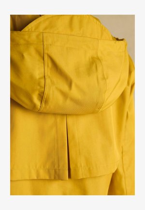 Žltá kapucňa s dizajnom s plisovaním na chrbte. Vyrobená z hladkej tkaniny s viditeľným stehom a zaoblenou kapucňou.