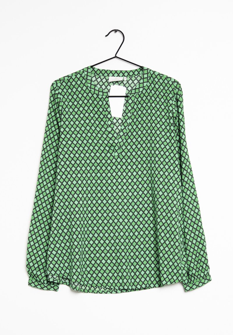 Blouse verte à manches longues avec motif de losanges noirs, col rond avec fente à l'avant, suspendue à un cintre noir sur fond blanc.