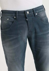 Vaqueros de mezclilla azul oscuro con corte recto, que cuentan con cinco bolsillos, botones de metal y un ligero desvanecimiento. La tela tiene una textura suave.