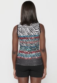 Meerkleurige mouwloze top met een zebra-patroon met strepen in zwart, wit, rood en blauw. De stof is glad met een lichte glans.
