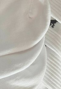 Weißer Strickstoff mit glatter Textur, der runde Formen in Schichten übereinander anzeigt. Dezent sichtbare Nähdetails.