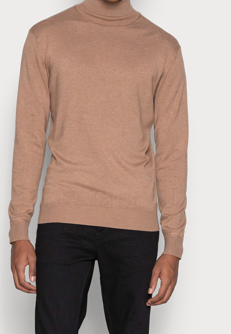 Polotröja i beige, tillverkad av mjukt stickat tyg. Figursydd modell med långa ärmar och ribbade muddar och fåll. Bärs med svarta byxor.