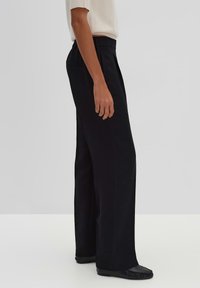 Hoge taille zwarte broek met brede pijpen, gemaakt van een gladde stof, met subtiele plooien en zijzakken, gecombineerd met platte schoenen.
