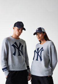 Grijze gebreide truien met een marineblauw NY-logo, voorzien van geribbelde manchetten en strepen. Een paar zwarte en marineblauwe honkbalpetten met logoprints.