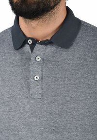 Grå polo skjorte med mørkegrå krage, tre knappestolper, teksturert stoff og kontrasterende knapper.