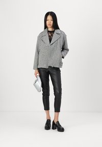 Veste de moto en mélange de laine grise avec fermeture éclair, pantalon en cuir noir et mocassins à plateforme noirs. Un sac à main argenté vient accentuer la tenue.