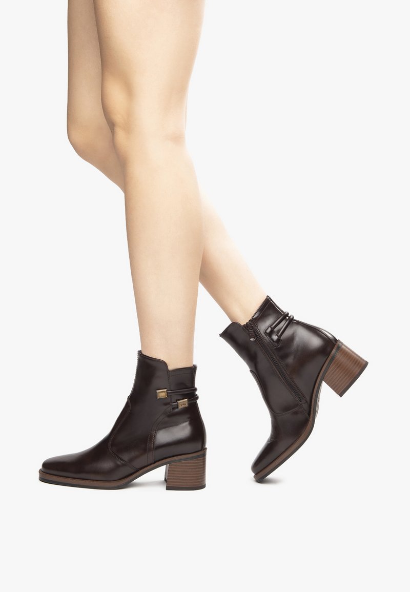 Bottines en cuir marron avec un talon carré, fermeture éclair latérale et accents décoratifs. La texture lisse et le design ajusté améliorent l'apparence.