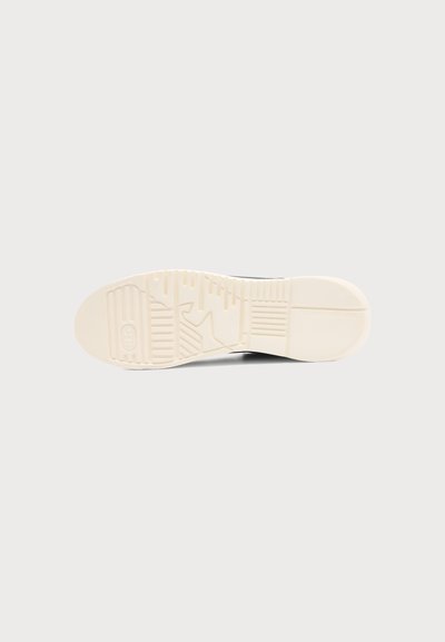 Semelle de chaussure de couleur beige clair, avec des motifs géométriques sur la bande de roulement et un logo près de la zone du talon sur un fond clair uni.