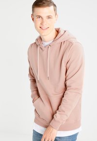 Lys rosa hettegenser laget av mykt stoff, med en frontlomme, justerbar snøring på hetta, og ribbede mansjetter og avslutning.