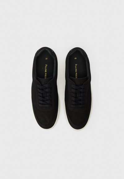 Melna zamšādas sporta apavi ar zemu profilu, ar apaļu purngalu, tonālām auklām un baltu gumijas zoli. Zelta uzraksts uz iekšējās zoles.