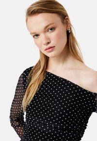 Sort off-shoulder kjole lavet af gennemsigtig stof med hvide prikker. Har lange ærmer, rynkede detaljer og en glat overflade.