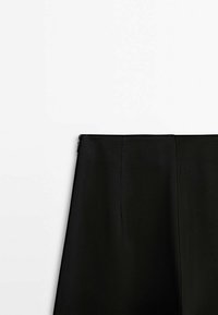 Jupe noire taille haute avec une fermeture éclair latérale, présentée sur un fond blanc uni.