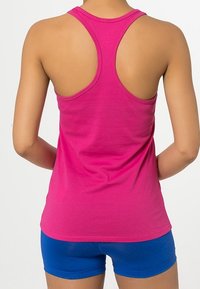 Růžový sportovní top s překříženými ramínky vyrobený z bavlny, s hladkým povrchem. V kombinaci s modrými sportovními šortkami. Jednoduchý design, bez vzorů nebo akcentů.