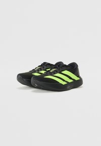 Schwarze Sport Schuhe mit grünen Streifen, mit einer glatten Textur, gepolsteter Sohle und einem niedrig geschnittenen Design, das sich gut zum Laufen eignet.