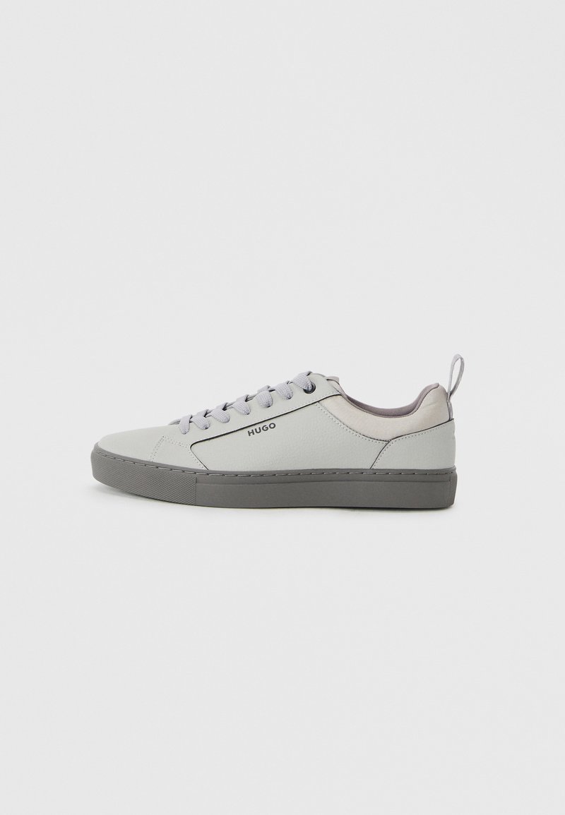 Light grey sneaker made of leather with a textured surface, featuring a grey rubber sole, grey laces, and a pull tab at the heel.