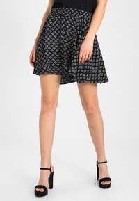 Falda negra con un patrón geométrico blanco, diseño acampanado y cintura elástica. Combinada con sandalias negras de tacón alto.