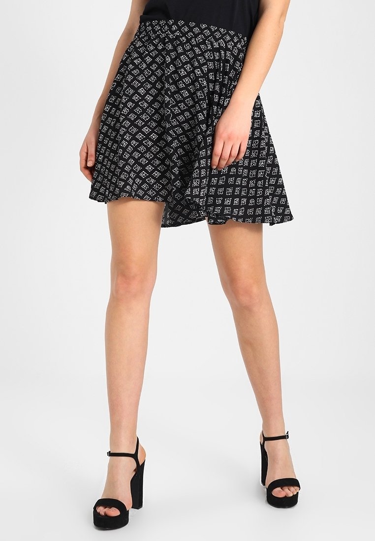 Falda negra con un patrón geométrico blanco, diseño acampanado y cintura elástica. Combinada con sandalias negras de tacón alto.