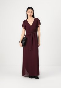 Burgundy maxi dress with a V-neck, flutter sleeves, and a tied waist detail; made of lightweight fabric with a flowing design.