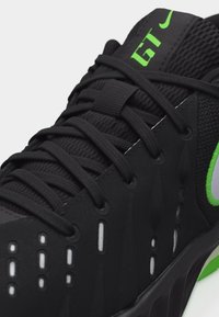 Czarne buty sportowe z zielonym logo "GT", czarnymi sznurowadłami, siateczkową cholewką oraz białymi akcentami wentylacyjnymi po bokach i na przodzie.