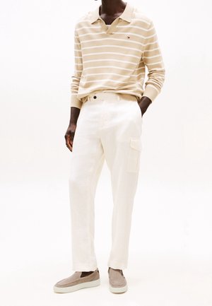 Beige and white striped long-sleeve polo shirt, paired with light linen cargo pants featuring a side pocket, and grey slip-on shoes.