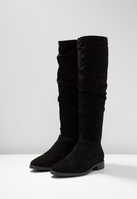 Knöchelhohe schwarze Wildlederstiefel mit einem lässigen Design, abgerundeter Spitze, flachem Absatz und glatter Oberfläche. Keine sichtbaren Beschläge oder Akzente.