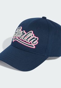 Navy baseball cap with raised white and pink embroidered text "Berlin." Features a structured design and a curved brim. Textured fabric surface.