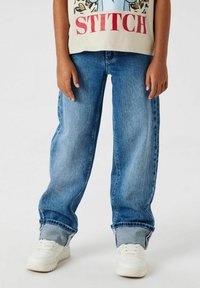 Ljust blå denimjeans med lös passform, med uppvikt fåll. Bärs med vita sneakers och en ljusfärgad t-shirt med tryck.