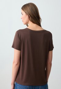 T-shirt corto marrone con scollatura rotonda. Realizzato in un tessuto morbido e liscio, presenta una vestibilità comoda. Dettagli di cucitura evidenti lungo l'orlo.