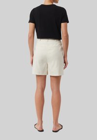 Czarny skrócony t-shirt zestawiony z kremowymi, dopasowanymi szortami. Szorty mają gładką teksturę i standardowe tylne kieszenie. Prosty krój.