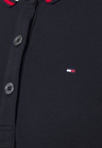 Marineblaues Polohemd aus strukturiertem Stoff mit Knopfleiste und roten Akzenten am Kragen; verfügt über ein kleines gesticktes Logo in Rot, Weiß und Blau.