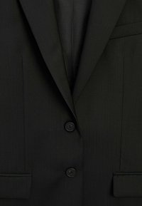 Sort skræddersyet blazer med to knapper, hakkraver og sidelommer. Stoffet har en subtil struktur, der fremhæver dets strukturerede udseende.