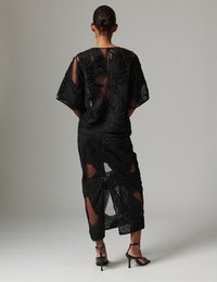 Σετ μαύρο διαφανές τοπ και φούστα με κυματιστό υφασμένο μοτίβο και κοψίματα. Ο σχεδιασμός περιλαμβάνει κοντά μανίκια και κομψή, εφαρμοστή σιλουέτα.