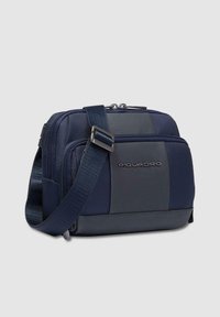 Bolso mensajero azul marino con nylon texturizado y acentos de cuero liso, que cuenta con una correa para el hombro y compartimentos con cremallera.