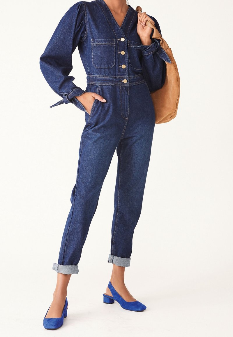 Combinaison en denim à manches bouffantes, poches avant, fermeture à boutons et revers retroussés, associée à des escarpins slingback en daim bleu.