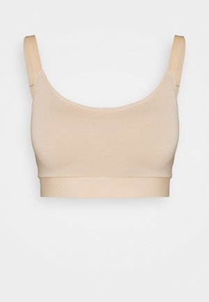 Beige stretch fabric bralette with adjustable straps, seamless design, and wide elastic band. Soft texture and smooth finish.