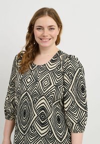 Voľná blúzka v krémovej farbe s odvážnym čiernym geometrickým vzorom. Obsahuje okrúhly výstrih a 3/4 dlhé nariasené rukávy. Mäkká textúra látky.