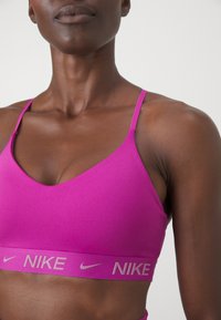 Sostén deportivo Nike en un vibrante color rosa, con tirantes finos y un escote en V. Acentuado con un logo en contraste en la banda. Textura suave.