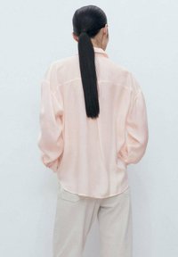 Camicia rosa chiaro a maniche lunghe con una vestibilità rilassata e un design leggermente over-size. Realizzata in un tessuto morbido e liscio con orlo arrotondato.