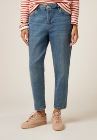 Vaqueros de mezclilla azul claro con un ajuste relajado, que cuentan con cinco bolsillos y un dobladillo con vuelta. Combinados con zapatillas de ante rosa claro.