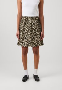 Krilo v leopardjem vzorcu v bež in črni barvi, s pregibnim dizajnom, srednje dolžine in pasom. Ujemajo se s črnimi loaferji in belimi nogavicami.