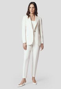 Biały, dopasowany żakiet i pasujące wąskie spodnie, wykonane z gładkiego materiału, z klapami i złotymi guzikami. Szpiczaste białe szpilki.