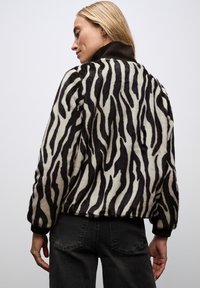 Veste en fausse fourrure avec un imprimé zèbre noir et blanc, dotée d'un col haut et de poignets côtelés, associée à un jean foncé.