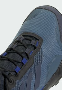 Blå och grå sportskor som har ett texturerat meshmaterial, svarta snören och gummidetaljer. Inkluderar mönstrad sidopaneldekor.