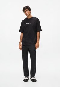 Črna bombažna majica s kratkimi rokavi in logotipom. Kombinirana s črnimi elegantnimi hlačami in masivnimi črno-belimi čevlji.