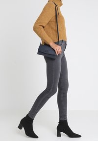 Šedé skinny džíny, pletený hořčicový rolák, černé kotníkové boty s špičatou špičkou a malá námořnická kabelka přes rameno.