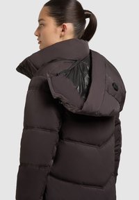 Chaqueta puffer marrón con cuello alto, que presenta un forro interior brillante, grandes secciones acolchadas y acentos de hardware negro.