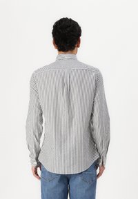 Striped long-sleeve shirt with a button-down collar; features narrow black and white stripes, a yoke seam, and rounded hem.