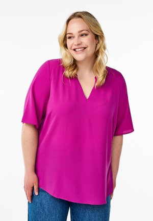 Fuchsia blouse met een V-hals en korte mouwen, met een relaxte pasvorm. De stof heeft een gladde textuur, gecombineerd met blauwe denim jeans.