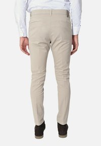 Pantaloni slim-fit beige chiaro con una texture liscia, due tasche posteriori e dettagli marroni. Abbinati a scarpe marroni scure.